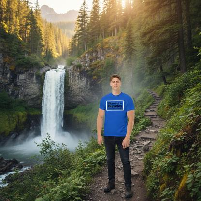 Person wearing a blue t-shirt with text standing in front of a waterfall in a forest.